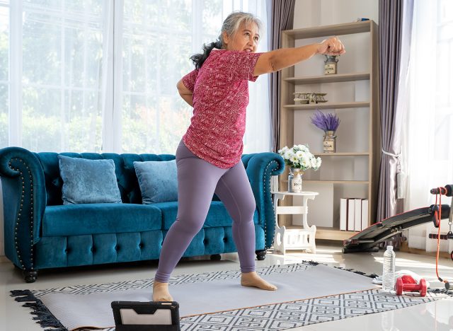 Senior woman exercise with standing and boxing jabs to side, she watch laptop for Training exercise online In Living Room During Quarantine