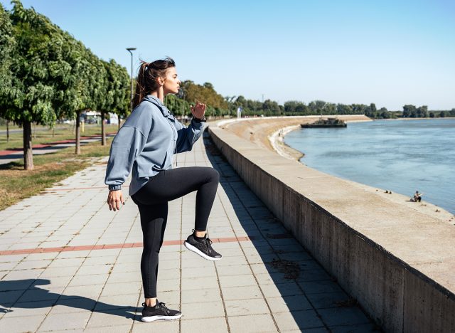 Young strong sexy muscular fit woman doing high knee skip running in the place as hard outdoor workout training in the autumn cold and sunny weather as preparation for marathon race