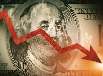 Closeup detail of dollar bill. Economist forecast for the United States. Glowing red arrow going downwards on Benjamin Franklin portrait on dollar bill. Effect of recession on US economy.