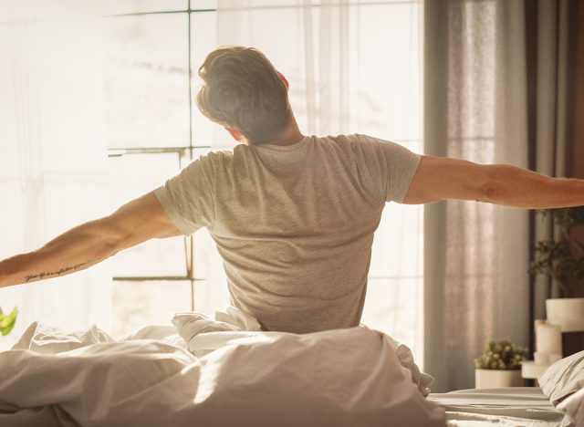 Handsome Young Man Waking up in the Morning, Stretches and Gets Out of Bed, Sun Shines From the Apartment Window in Bedroom, He is Ready for Business Opportunities, Achievements, Adventures