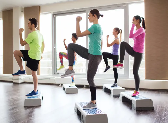 fitness, sport, training, aerobics and people concept - group of people working out with steppers in gym, step ups