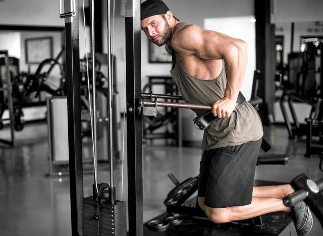 Attractive young adult man doing dips exercise in modern fitness center. Toned image.