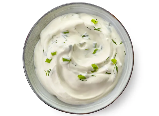 Bowl of sour cream sauce with herbs isolated on white background, top view