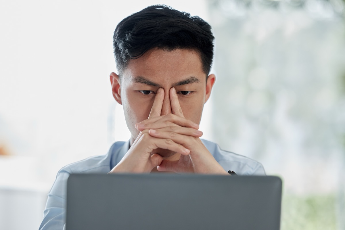 Asian man, laptop and headache with stress in mistake, debt or financial crisis from stock market crash. Businessman or frustrated broker with migraine on computer in burnout, anxiety or depression