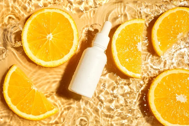 Unbranding dropper bottle with beauty serum or essential oil and orange citrus slices in splashing water background, top view. Moisturizing organic vitamin C brightening skin care product.