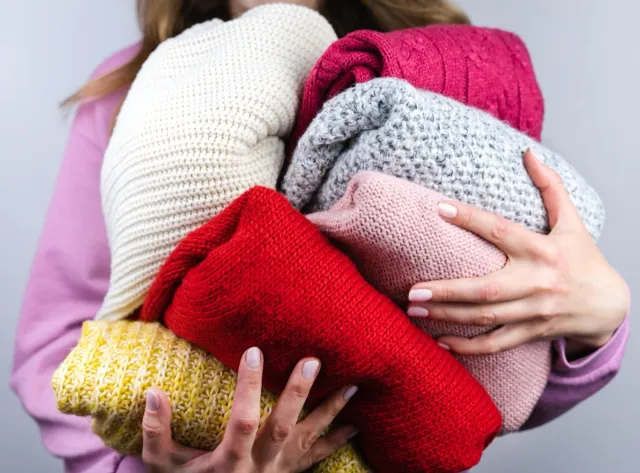 A woman holds bright warm winter sweaters. Closet cleaning. Donations. Close-up. Selective focus.