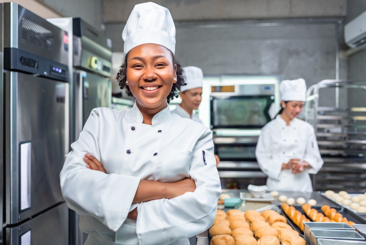Smiling african female bakers looking at camera..Chefs baker in a chef dress and hat, cooking together in kitchen.Team of professional cooks in uniform preparing meals in the kitchen.