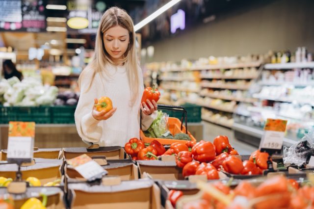 Customer comparing yellow and red bell peppers while shopping for groceries in a supermarket