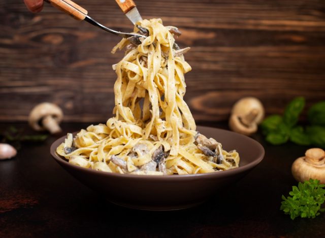Homemade Italian fettuccine pasta with mushrooms and cream sauce (Fettuccine al Funghi Porcini). Traditional Italian cuisine. Served on a dark table with a rustic wooden background. Close-up