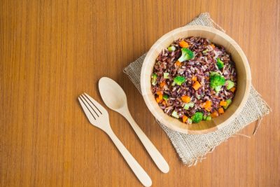 Vegetarian fried rice dish of red brown jasmine rice and riceberry with diced fresh broccoli and carrot in wooden bowl over natural sackcloth on wood table, healthy dish concept (top view, flat lay)