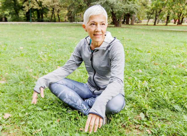 Senior Woman Relax After Exercise In Nature, Old Woman Sitting On Green Grass At The Park.