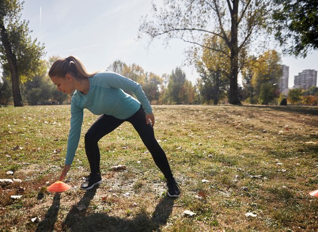 woman, cardio exercise in public park, between two fitness props, Lateral Shuffle, outdoors, sunny autumn day.