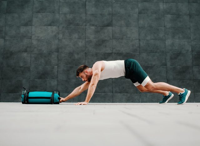 Side view of handsome fit muscular caucasian man doing inchworms with training bag.