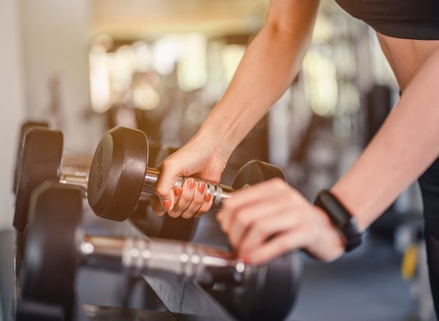 fitness ,workout, gym exercise ,lifestyle and healthy concept. Close-up hands women exercise by dumbbells at the indoor gym for good health at sunset.