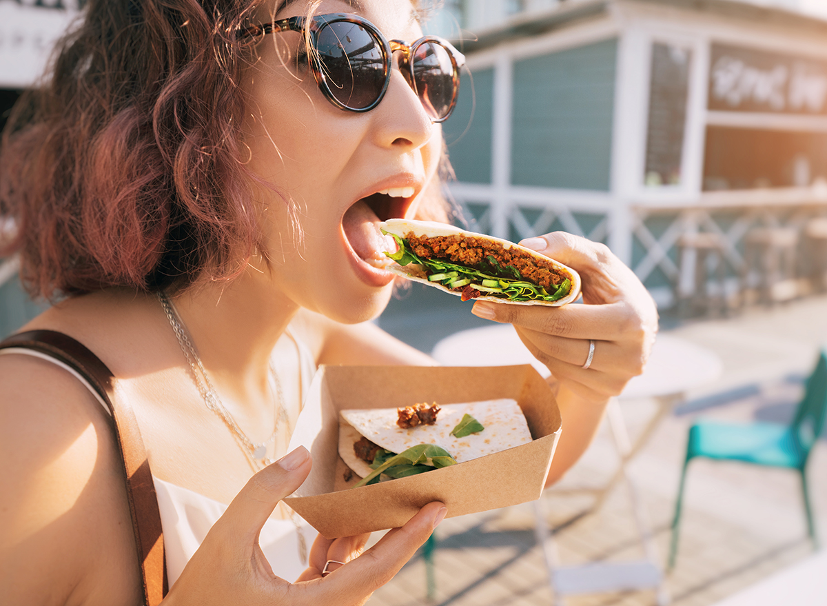 Happy woman eats a fast food flatbread with filling sitting on the street and resting after a working day. Concept of healthy food and extra calories
