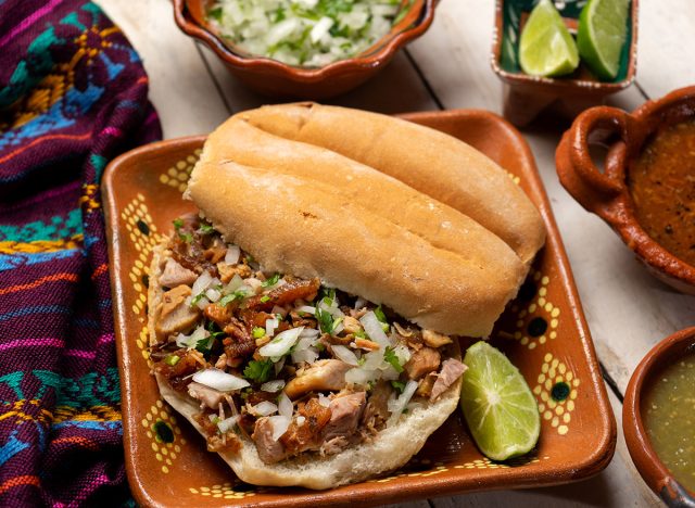 Confit pork sandwich called Torta de carnitas on white background. Traditional Mexican food