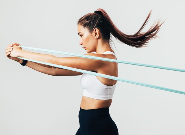 Side view of sportswoman exercising with resistance band against white wall