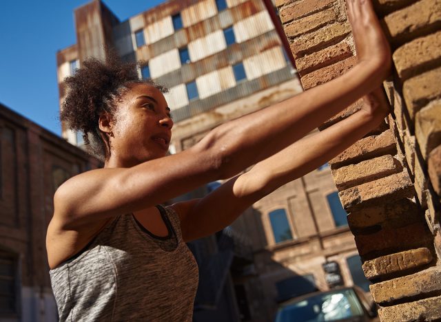 Sporty young black woman doing wall push ups while working out alone outdoors during the day