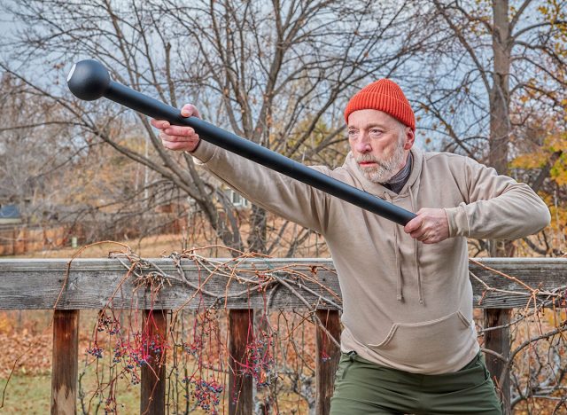 senior man (in late 60s) is exercising with a steel mace in his backyard, fall scenery