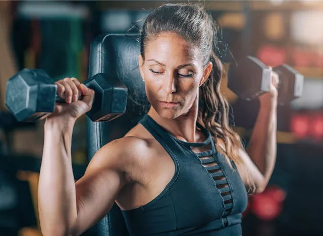 Female Athlete Exercising with Dumbbells in the Gym. Strength Training.