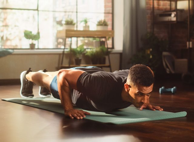 Strong Athletic Black Man Does Workout at Home Gym, Doing Push Ups. Lean Fit Muscular Mixed Race Sportsman Staying Healthy, Training at Home. Sweat and Determination. Wide Shot