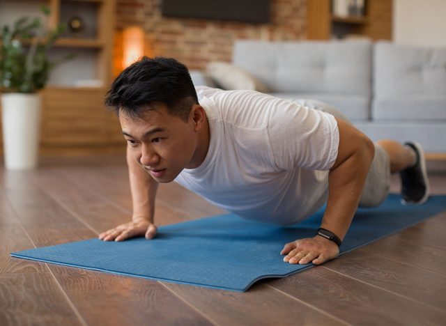 Strong asian mature man making strength workout, doing push ups on sports mat, having domestic workout. Sporty korean male training his body, leading active lifestyle