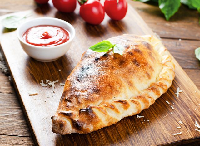 Delicious Pizza Calzone, Traditional Italian Pizza with Tomatoes and Fresh Basil on Wooden Rustic Background