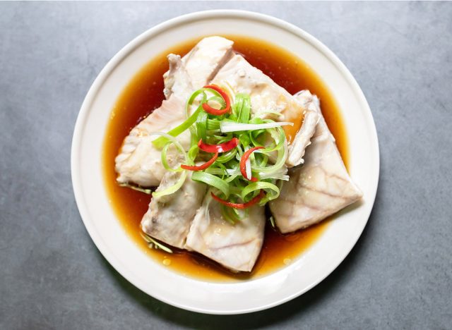 Sea bass fillet steam with soy sauce. Top view on black table background.