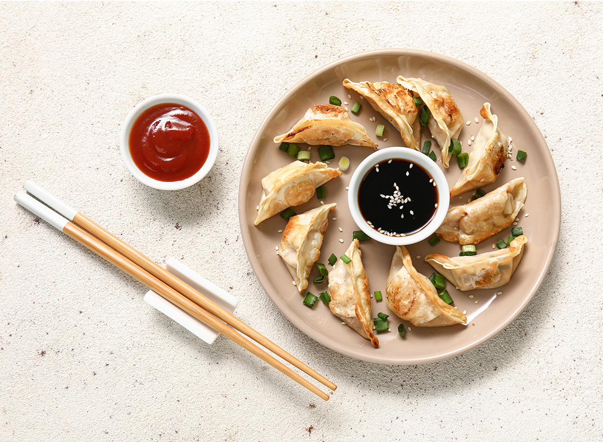 Plate with fried Japanese gyoza and bowl of soy sauce on white background