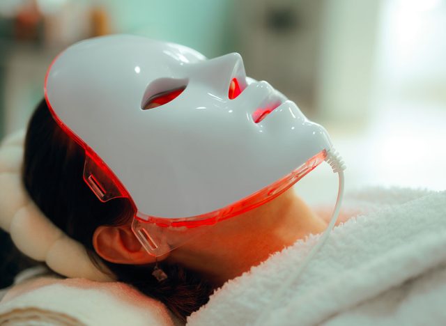  Woman Getting Red Light Therapy for her Skin with Mask. Lady using professional services in a beauty salon for skin care 