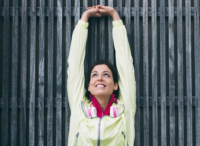 Fitness woman stretching arms and back against a wall. Female athlete working out and exercising outside.