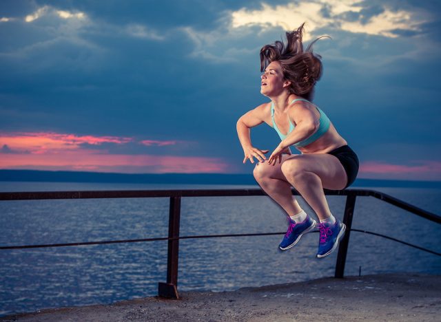 Young woman in sportswear doing plyometric exercises on sea dock. Fitness workout outdoors.