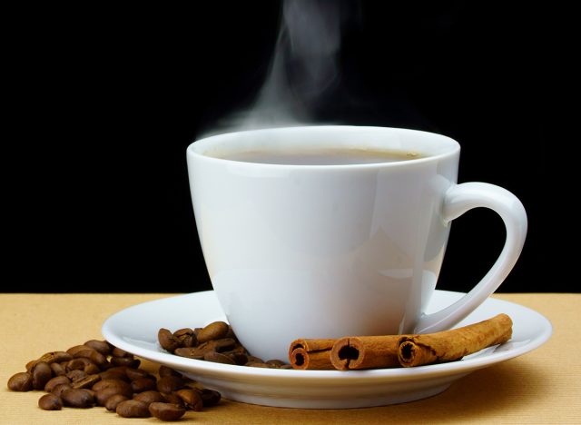 Mug of coffee with beans and cinnamon on black background
