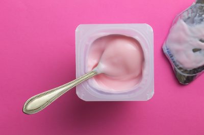 Strawberry pink yogurt in plastic cup with spoon and foil lid isolated on pink background - top view photo
