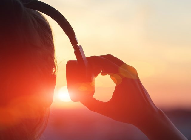 Girl in headphones listening to music in the city at sunset