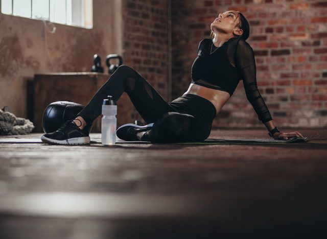 Tired woman having rest after workout. Tired and exhausted female athlete sitting on floor at gym with a water bottle.