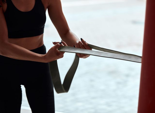 Cropped fit female in sportive topic pulling rope in gym. Window background