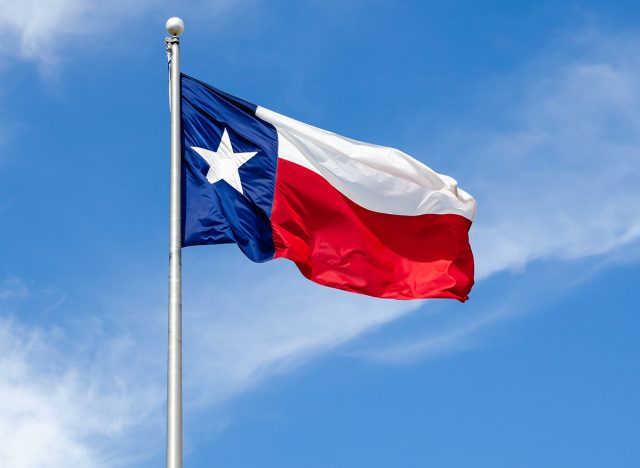 Texas State flag on the pole waving in the wing against blue sky and white clouds