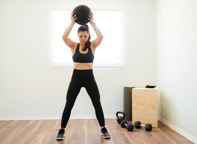 Athletic woman in her 30s with strong arms and a toned body throwing a medicine ball during her functional training at home