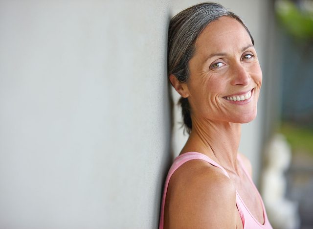 Happiness is an inside job. Portrait of an attractive mature woman in gymwear leaning against a gray wall.