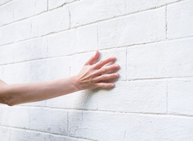 Woman's hand on the background of a white brick wall. A woman touches the old wall of the monastery.