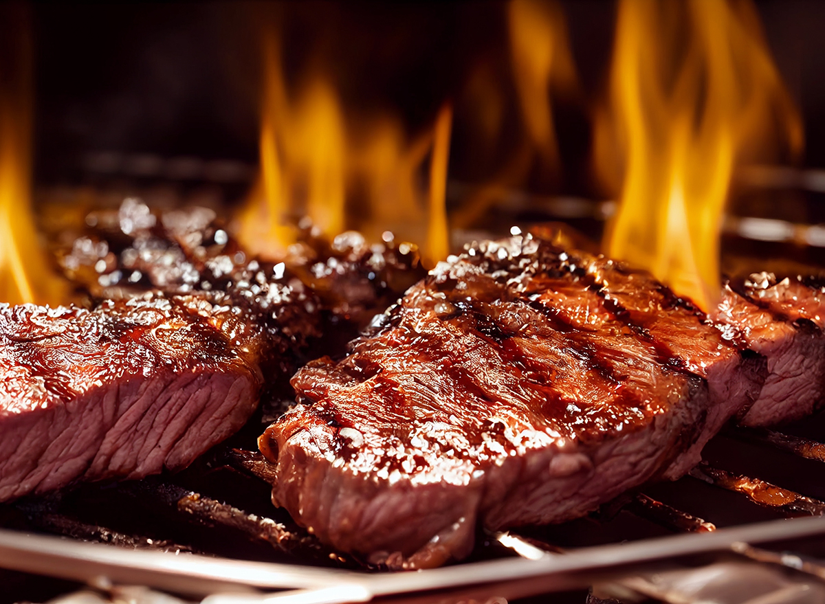 Grilled meat steak on stainless grill depot with flames on dark background.