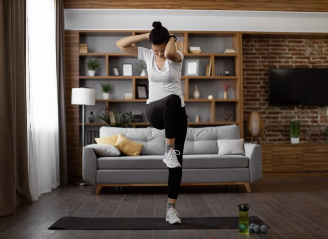 Active young brunette in sport clothes standing on yoga mat and making criss cross crunches exercise. Multiracial healthy woman training abs during domestic workout.