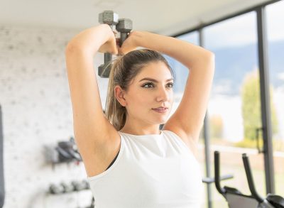 young girl exercising her forearms with dumbbells in a gym. Overhead Triceps Extensions