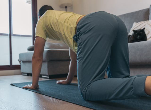 Anonymous Man Stretching on Mat with Laptop for Online Class in Home Setting. Unrecognizable man does yoga stretches on mat with laptop nearby for online class in cozy home environment.
