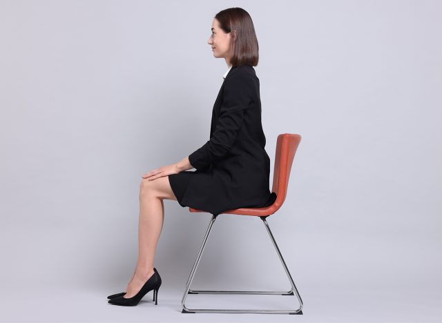 Woman with good posture sitting on chair against gray background