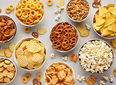 Set of many bowl with different salty snacks on light gray background. Chips, popcorn, nuts, nachos and pretzels. Party food. Top view