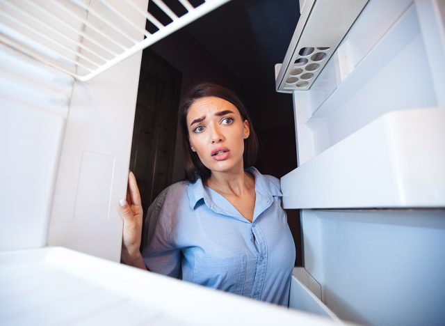 Young shocked woman looking in empty fridge at home, view from inside