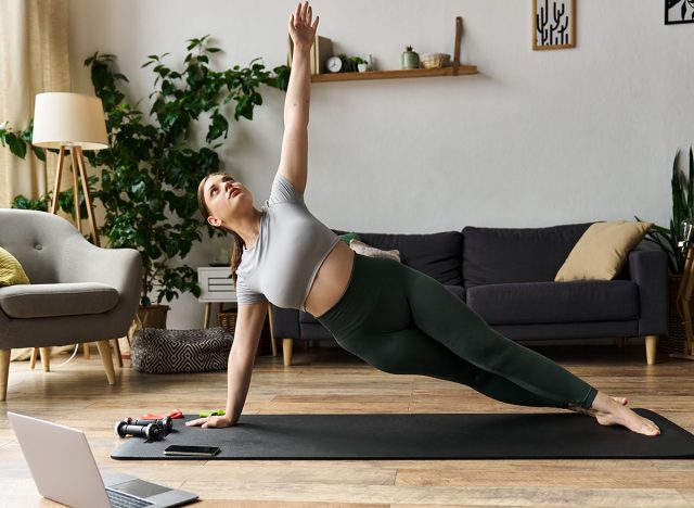 A dedicated woman in active wear focuses on her side plank workout, bringing energy to her home routine.