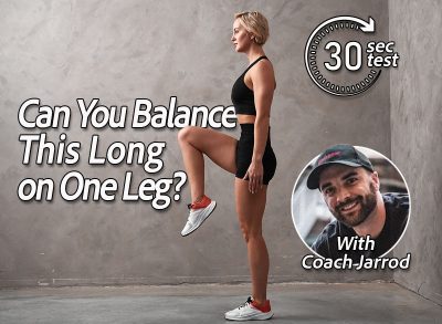 Coach Jarrod. Standing exercise lifting leg with bent knee hands lowered pressed against the body. A young woman of athletic build is engaged in fitness.